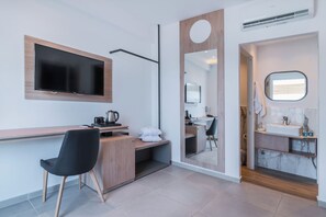 A modern hotel room with a flat-screen TV, a desk with a coffee maker, a black chair, a large mirror, and a bathroom with a marble sink. - Kahlua Boutique Hotel (Hersonissos)