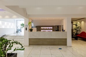 A hotel reception area with a marble reception desk, a red chair, and a potted plant. - Kahlua Boutique Hotel (Hersonissos)