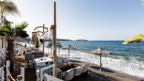 Une terrasse en bord de mer, avec des tables et des chaises, des parasols et une vue sur la mer.