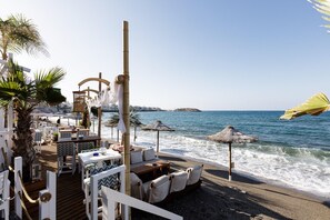 Eine Strandterrasse mit Tischen, Stühlen und Sonnenschirmen, mit Blick auf das Meer.