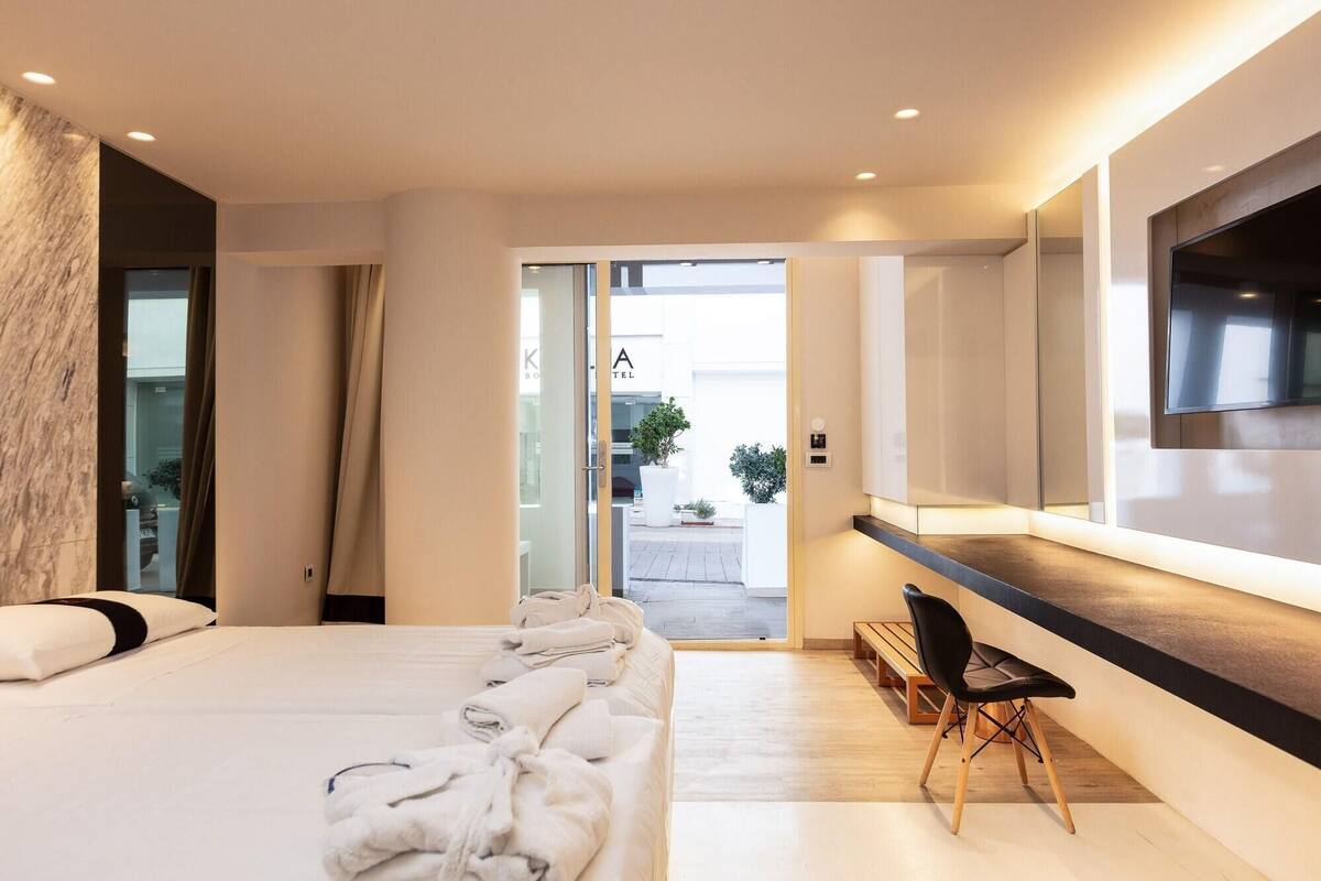 A modern hotel room with a large bed, a desk with a chair, a TV, and a view of the outside.