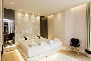 A modern bedroom with a large bed, a black chair, and a marble wall. - Kahlua Boutique Hotel (Hersonissos)