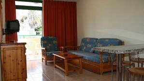 Ein Wohnzimmer mit einer Couch, Sesseln, einem Holztisch und einem Fernseher.