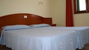 Ein Doppelbett mit Holz-Kopfteil, ein Nachttisch, eine Wandleuchte und ein Fenster mit roten Vorhängen.