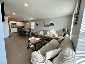 A modern living room with a sofa, coffee table, and a dining area with chairs and a table.