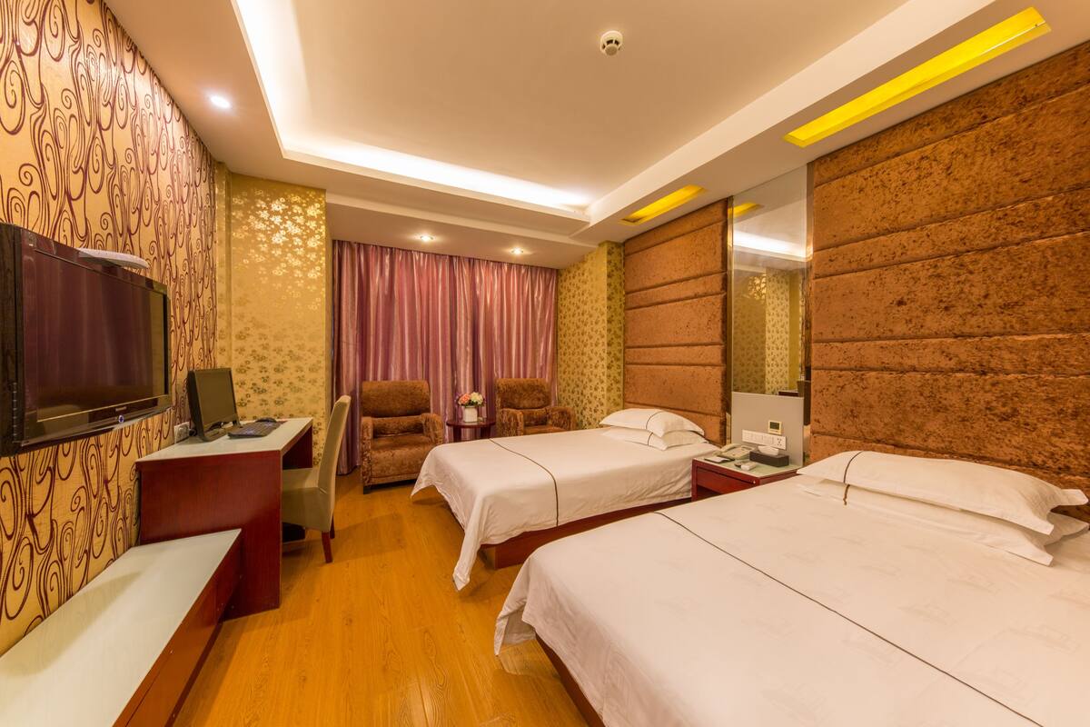 A hotel room with two beds, a desk, a TV, and a seating area with chairs.