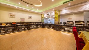 A buffet area with a marble countertop, a chef at work, and a seating area with a red chair. - Yiwu Chuzhou Hotel (Jinhua)
