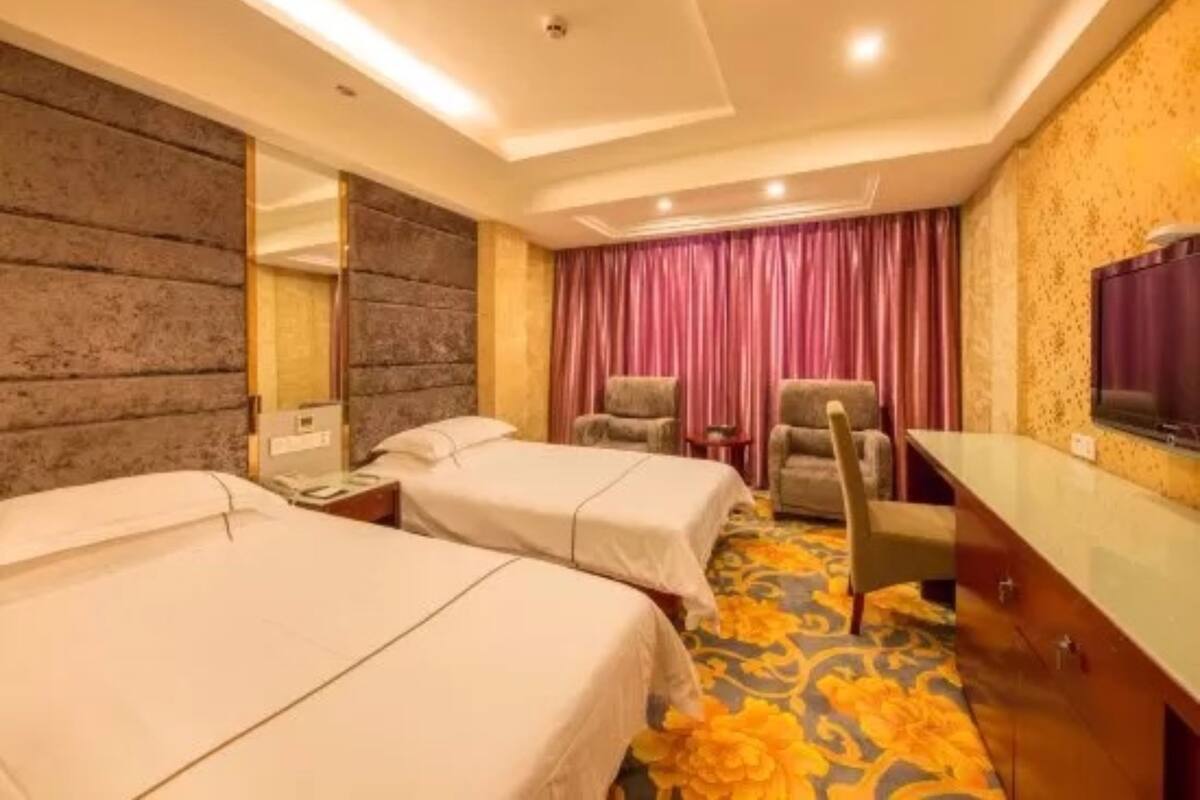 A hotel room with two beds, a desk, a chair, a television, and a mirror.