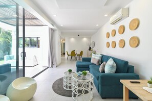 Una sala de estar moderna con un sofá color turquesa, una mesa de centro de vidrio y una zona de comedor con sillas amarillas.