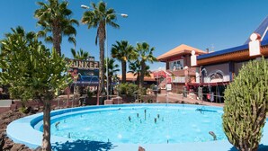 Une piscine entourée de palmiers et de bâtiments portant des enseignes.
