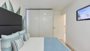 A bedroom with a bed, pillows, a TV, and a door leading to another room.