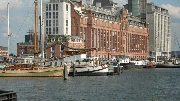A waterfront building with a traditional architectural style, featuring a prominent red brick facade and a tall tower. - Cozy and romantic apartment in captain's steering cabin (Amsterdam)