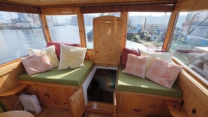 A wooden cabin with a bench seating area, a small table, and a view of the water and boats. - Cozy and romantic apartment in captain's steering cabin (Amsterdam)