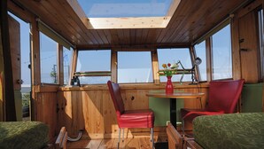 A wooden cabin with a skylight, two red chairs, a small table, and a bed with green bedding. - Cozy and romantic apartment in captain's steering cabin (Amsterdam)