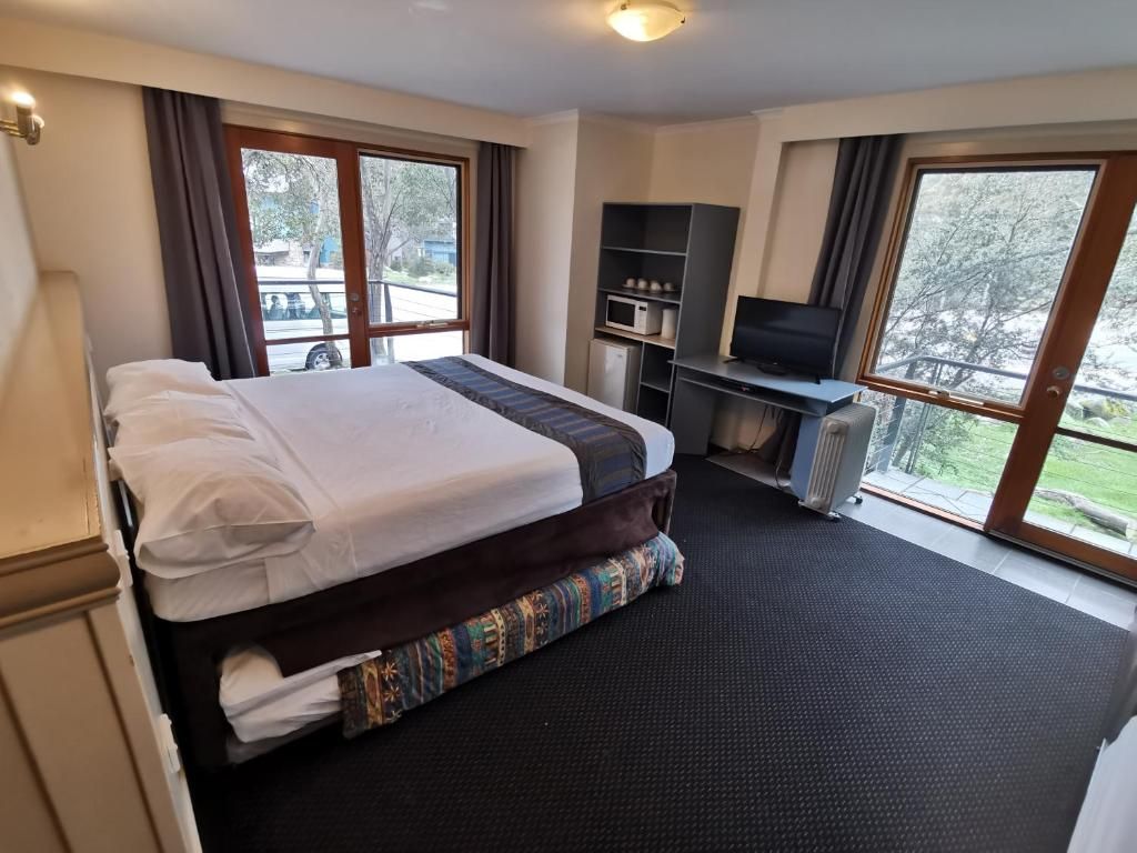 A hotel room with a bed, a desk with a computer, a TV, and large windows.