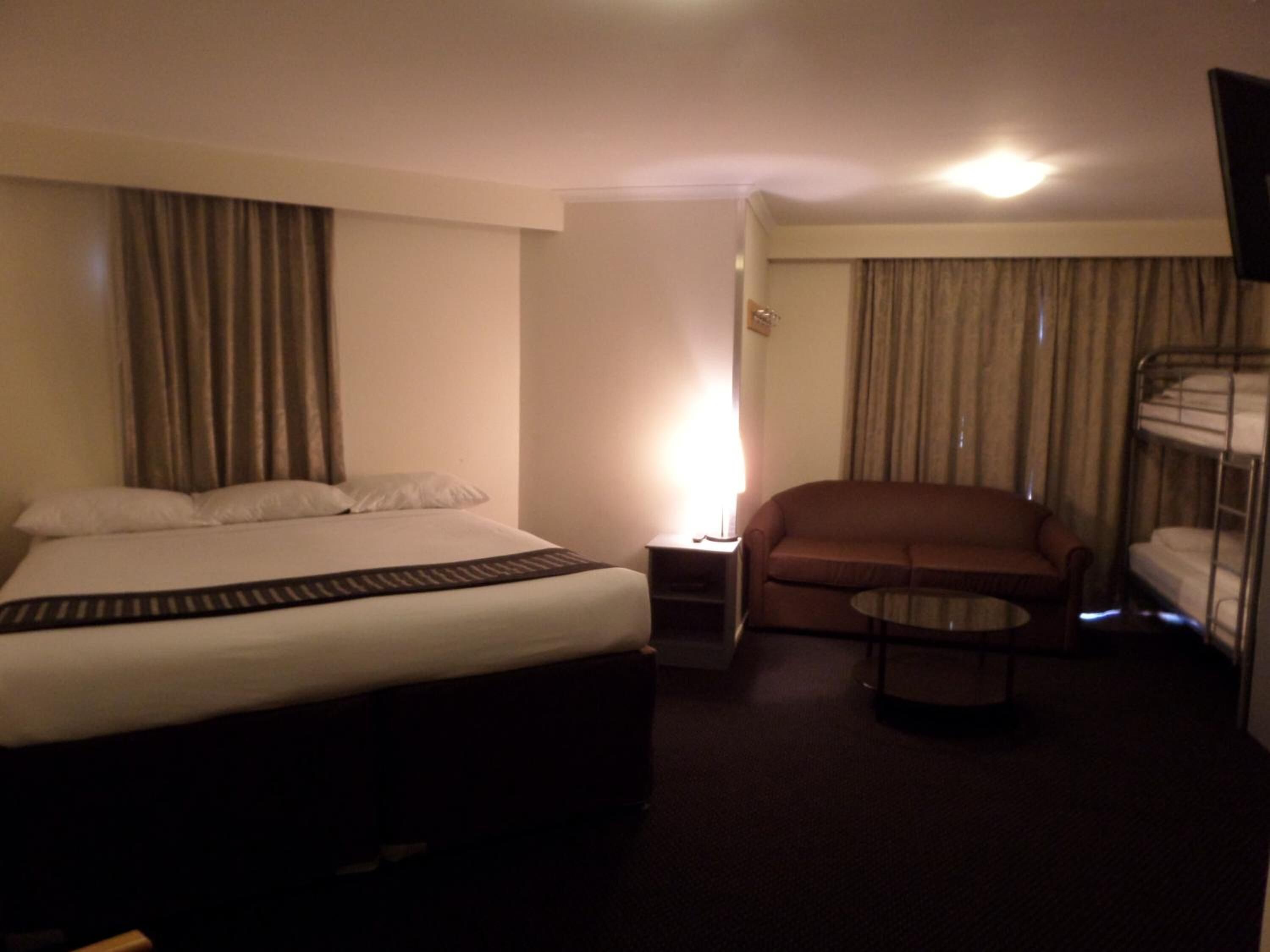 Ein Hotelzimmer mit einem Bett, einem Schlafsofa, einem kleinen Tisch, einer Lampe und einem Etagenbett.