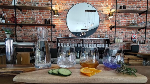 A bar area with a wooden counter, glasses of water and gin, and a large mirror on the brick wall. - The River Inn Thredbo (Thredbo)