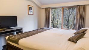 A hotel room with a bed, a TV on a desk, and a window with curtains. - The River Inn Thredbo (Thredbo)