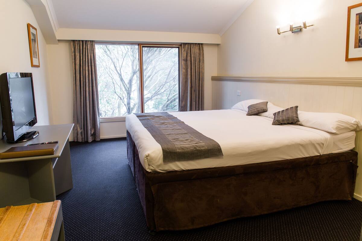 A hotel room with a large bed, a desk with a computer, and a window with curtains.