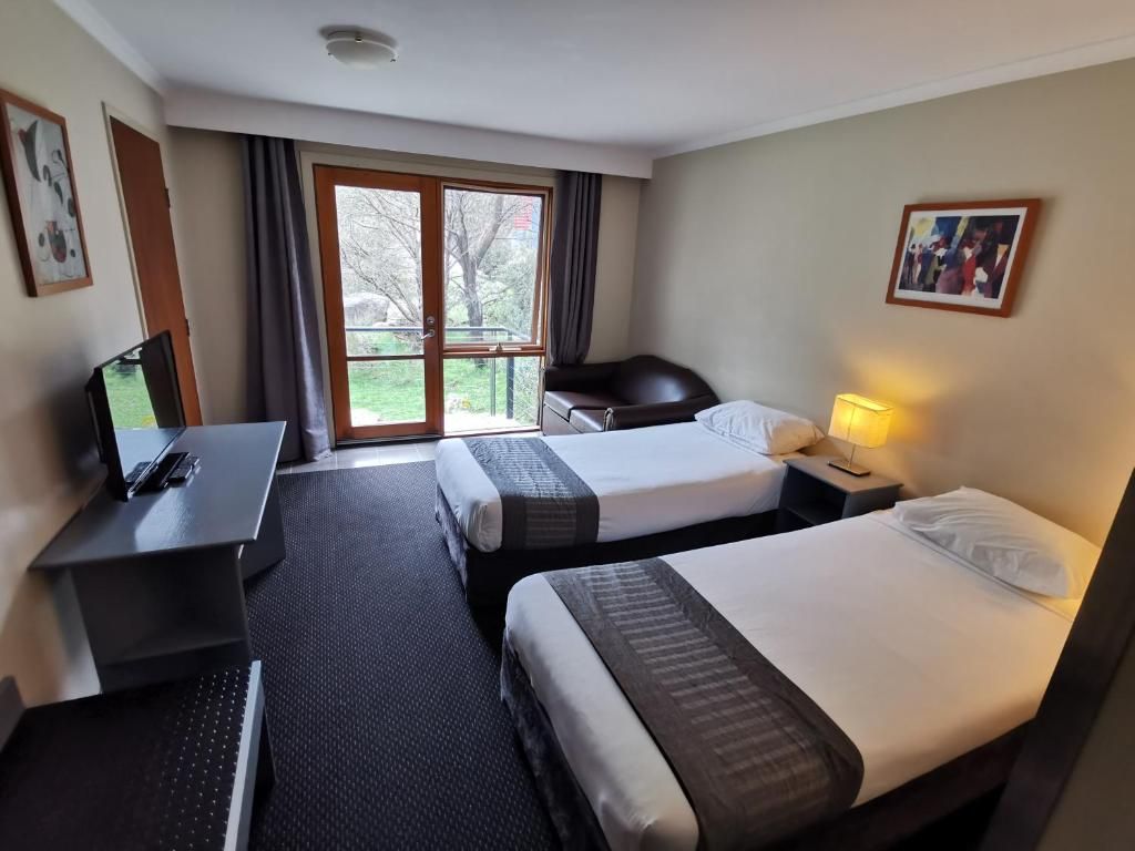 A hotel room with two beds, a desk, a chair, a laptop, and a window with curtains.