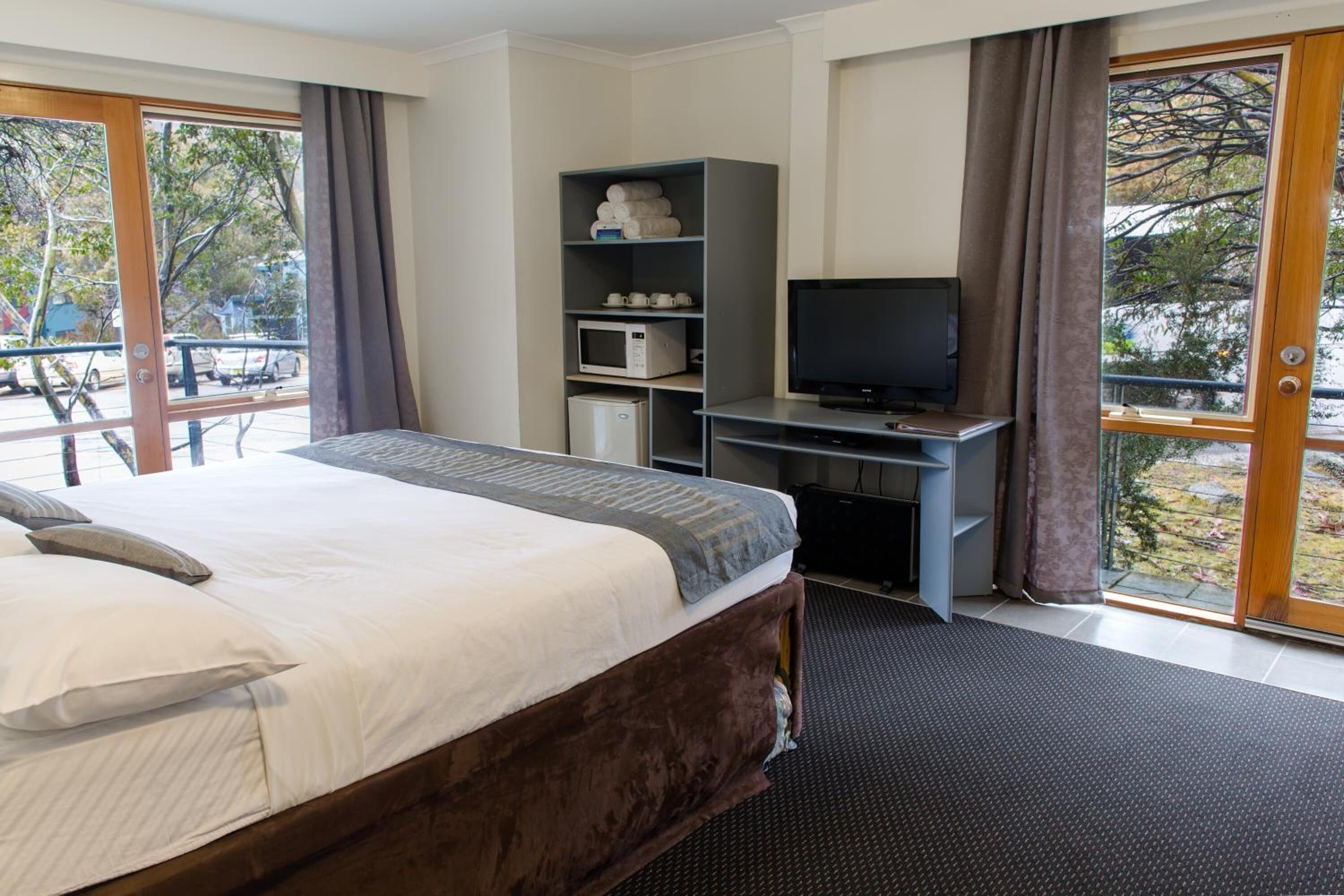 A hotel room with a bed, a desk with a television, a microwave, and a shelf with towels.