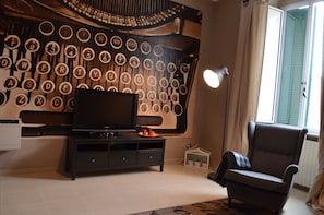 A living room with a television on a black stand, a black sofa, and a wall with circular patterns.