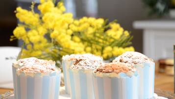 A table with cupcakes in striped paper cups, a vase of yellow flowers, and a white cabinet in the background.