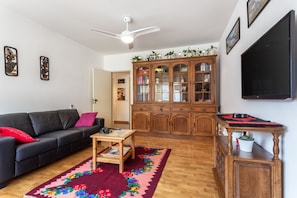 A living room with a black leather sofa, a wooden coffee table, a red and black rug, a wooden cabinet with glass doors, and a ceiling fan.
