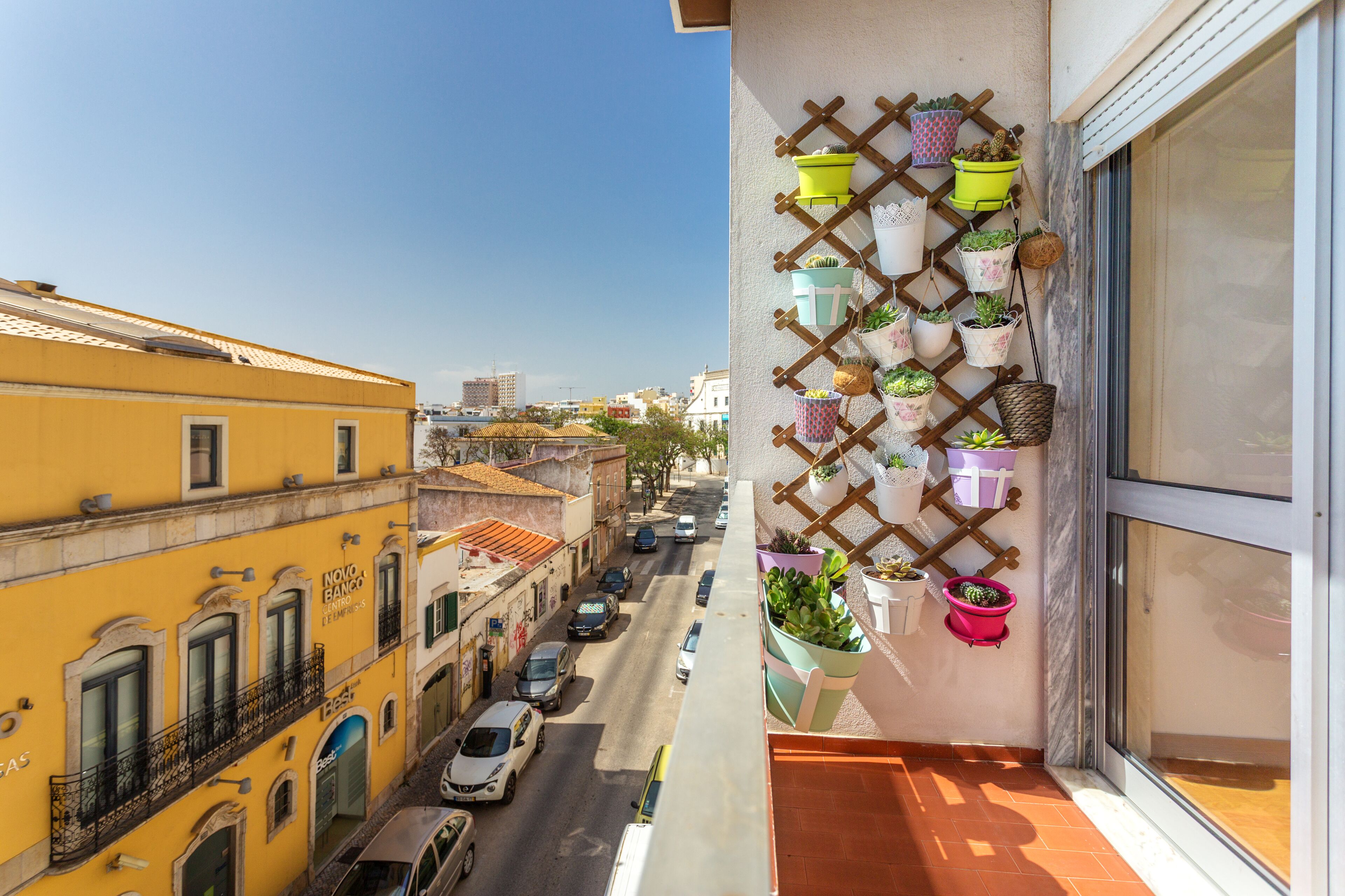 A balcony with a view of a street, potted plants, and a building facade.