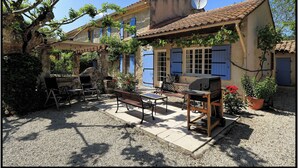 Een landelijke woning met een terras, zitplaatsen buiten en een barbecue.