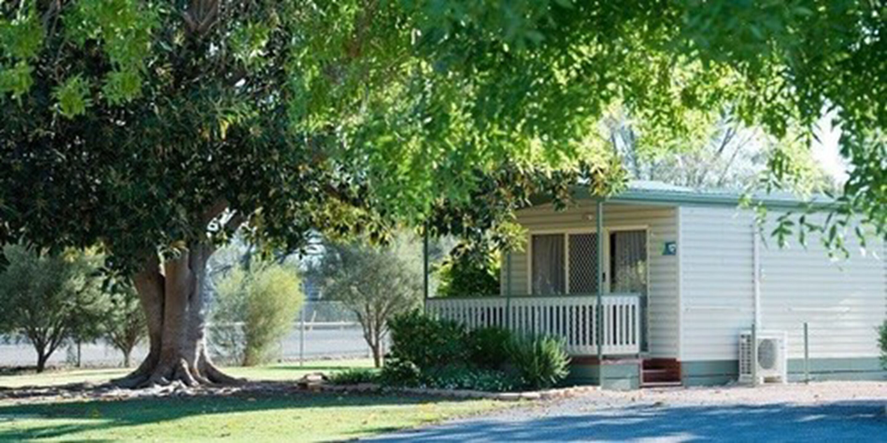 A single-story mobile home with a porch, surrounded by trees and a grassy yard.