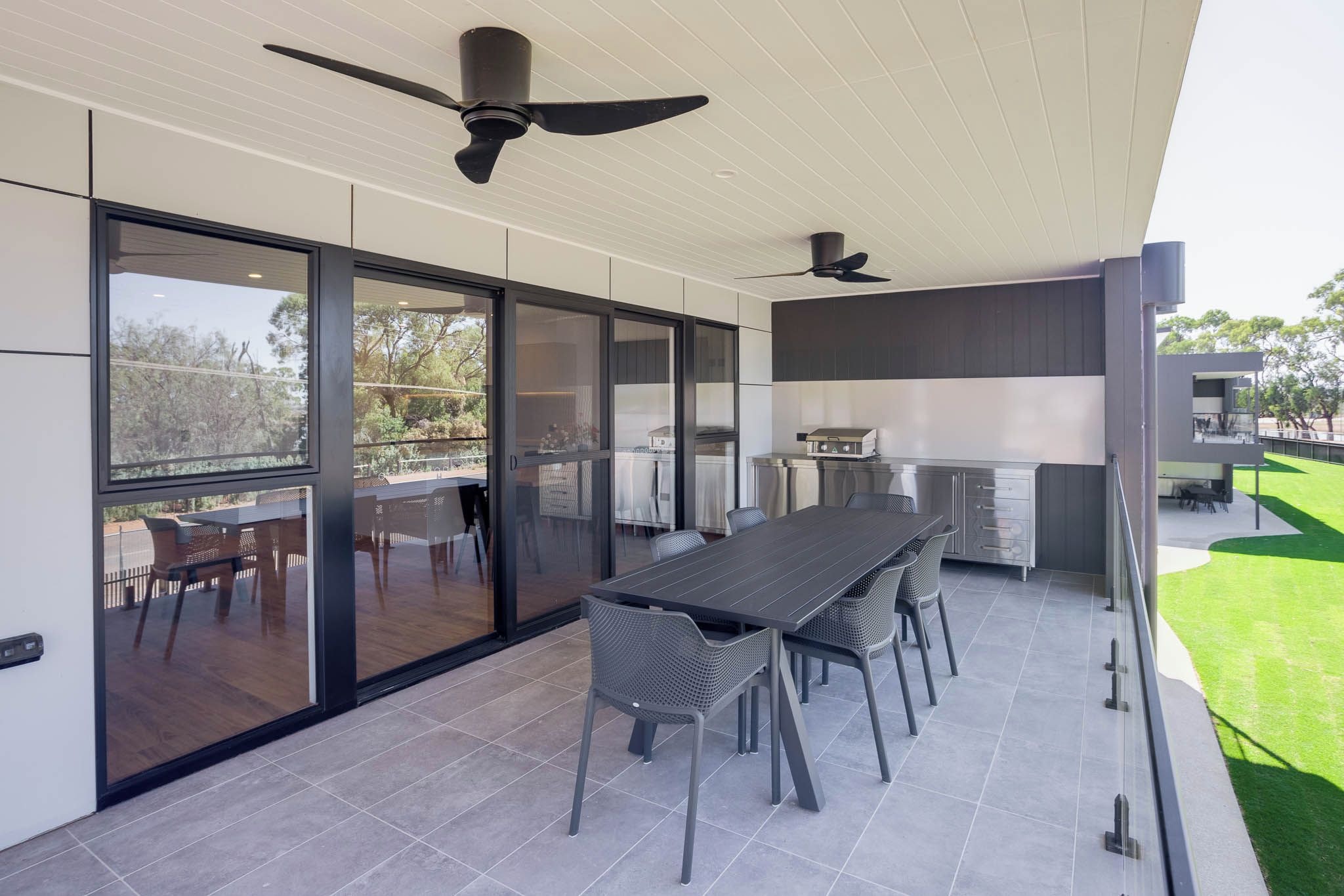 A modern kitchen with a dining area, large windows, and ceiling fans.
