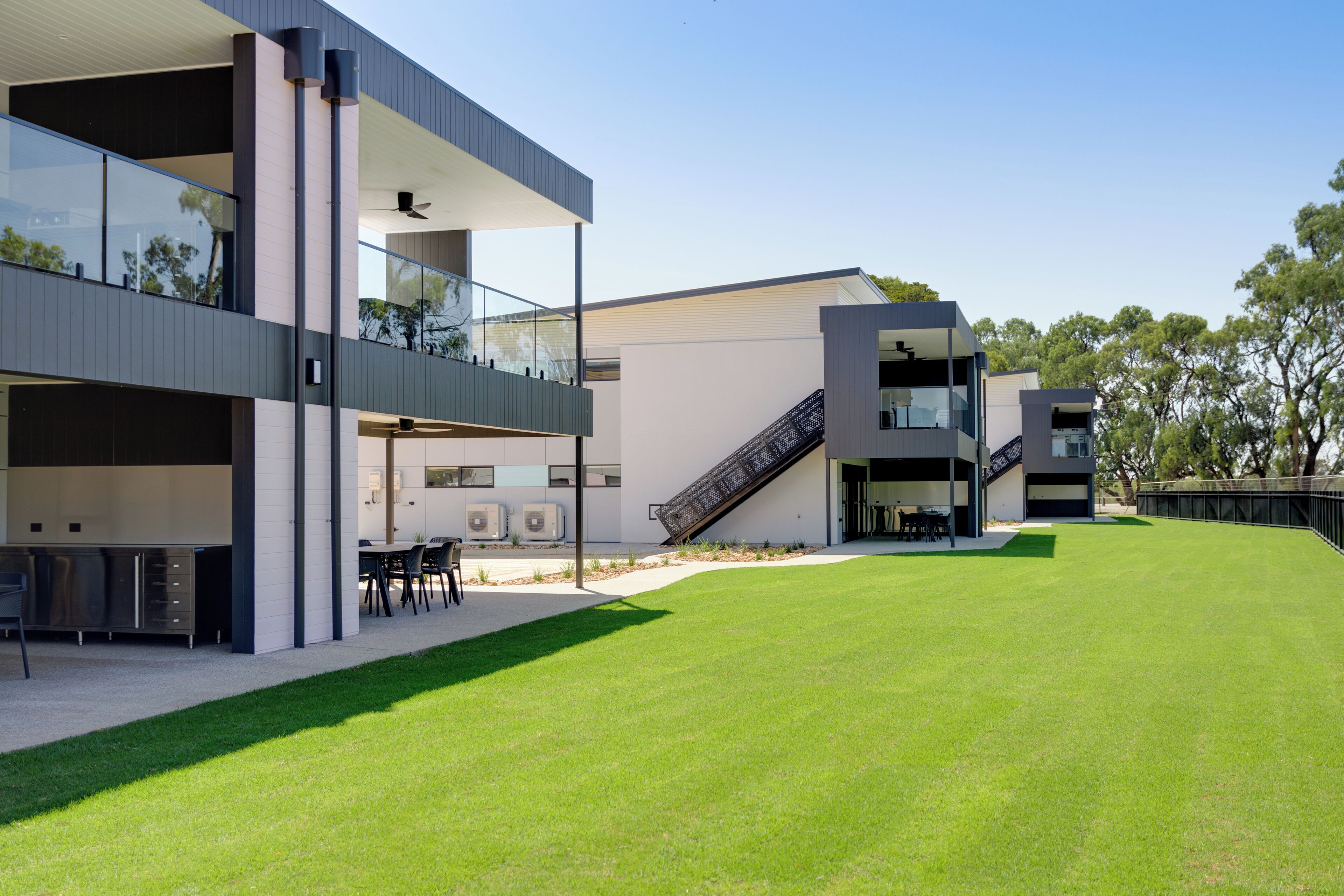 A modern multi-story building with a flat roof, a covered outdoor seating area, and a grassy courtyard.