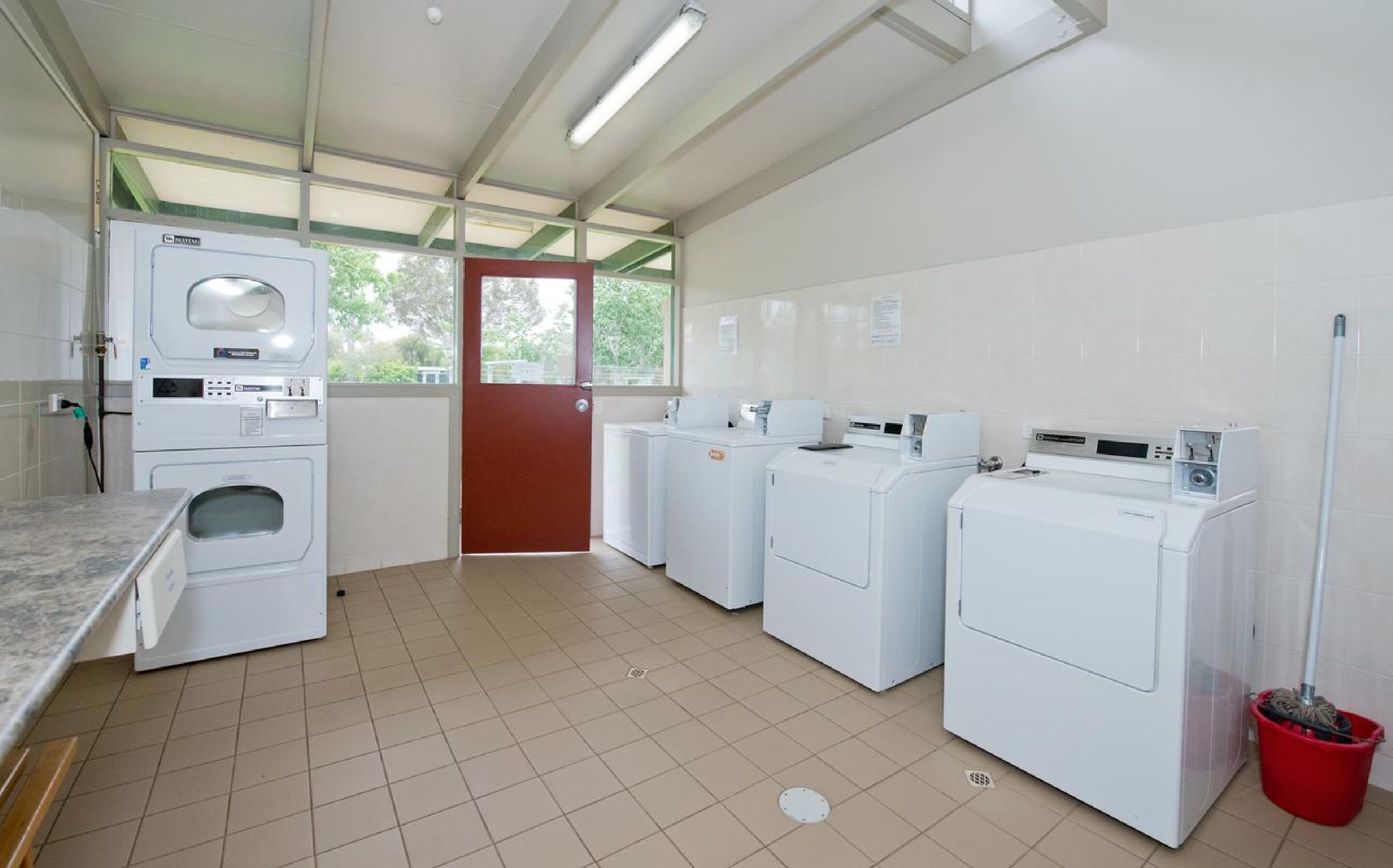 Een wasserij met vier wasmachines, een rode deur en een betegelde vloer.