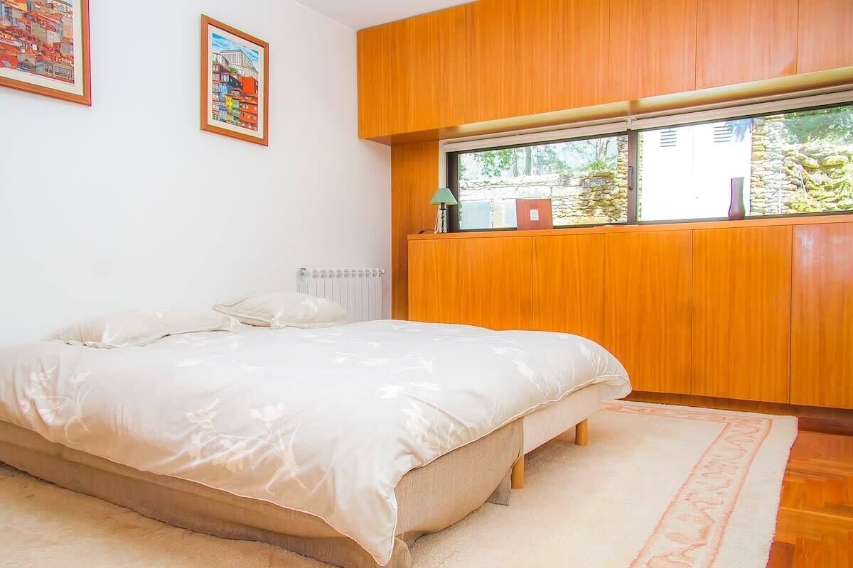A bedroom with a bed, wooden paneling, a window, and two framed pictures on the wall.