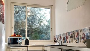 Eine kompakte Küche mit Geschirrspüler, Backofen und Fenster mit Blick auf einen Baum.