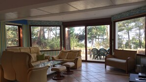 Ein sonnendurchfluteter Raum mit Ledersofas, einem Glastisch und Blick auf eine Terrasse mit Gartenmöbeln.