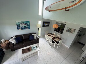 A living room with a brown leather sofa, a white coffee table, and a dining area with a white table and chairs.
