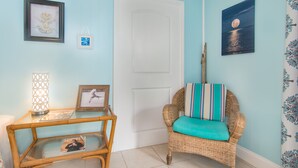 A room with a wicker chair with a teal cushion, a glass table with magazines, and framed artwork on the walls. - BOUTIQUE BUNGALOW. INTIMATE TROPICAL SETTING. STEPS TO BEACH ACCESS. (Juno Beach)