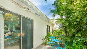 A covered outdoor patio with a table and chairs, surrounded by lush greenery. - BOUTIQUE BUNGALOW. INTIMATE TROPICAL SETTING. STEPS TO BEACH ACCESS. (Juno Beach)