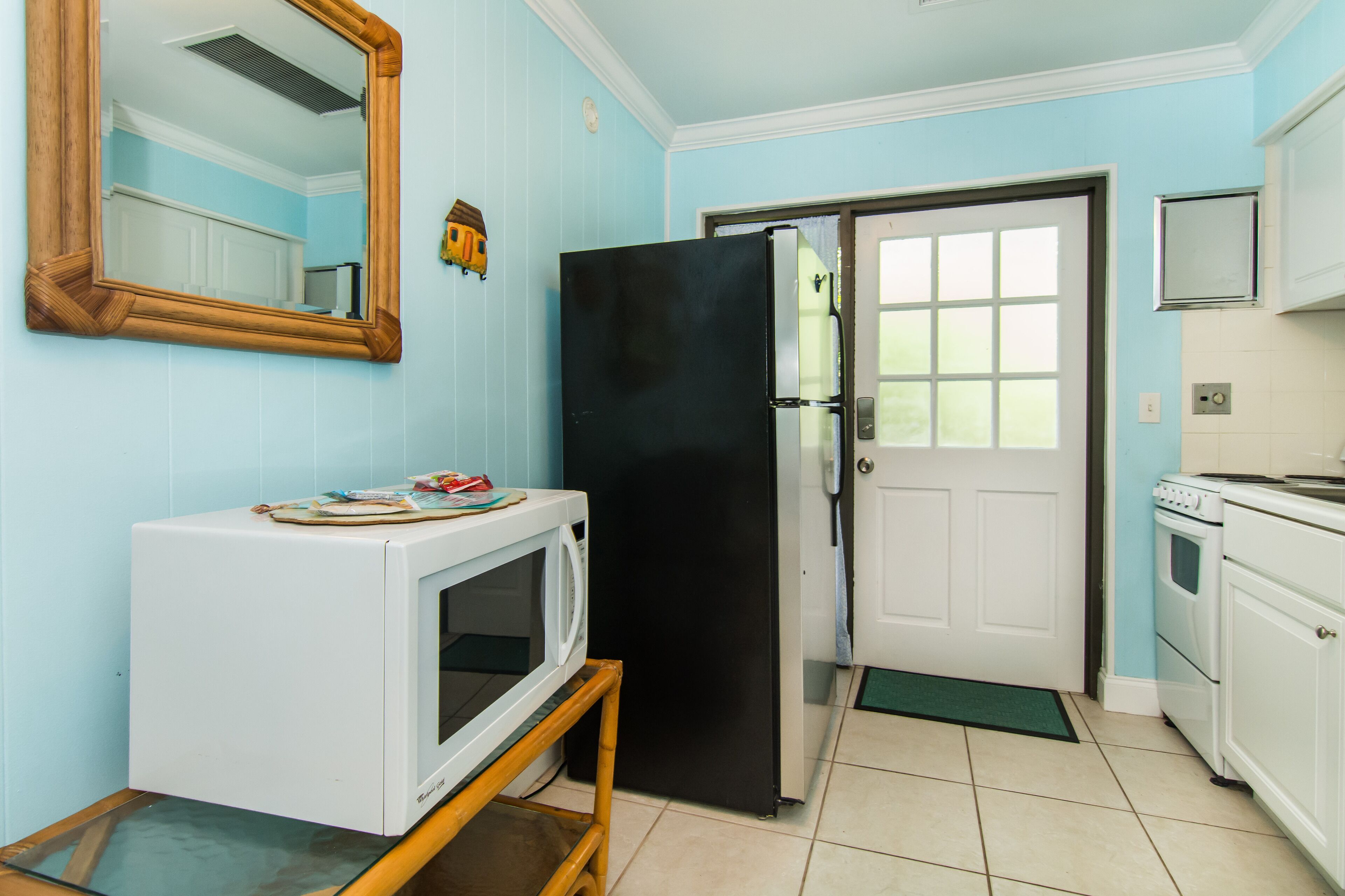 A kitchen with a white refrigerator, a microwave on a wooden stand, a black freezer, a white oven, and a door with a window.