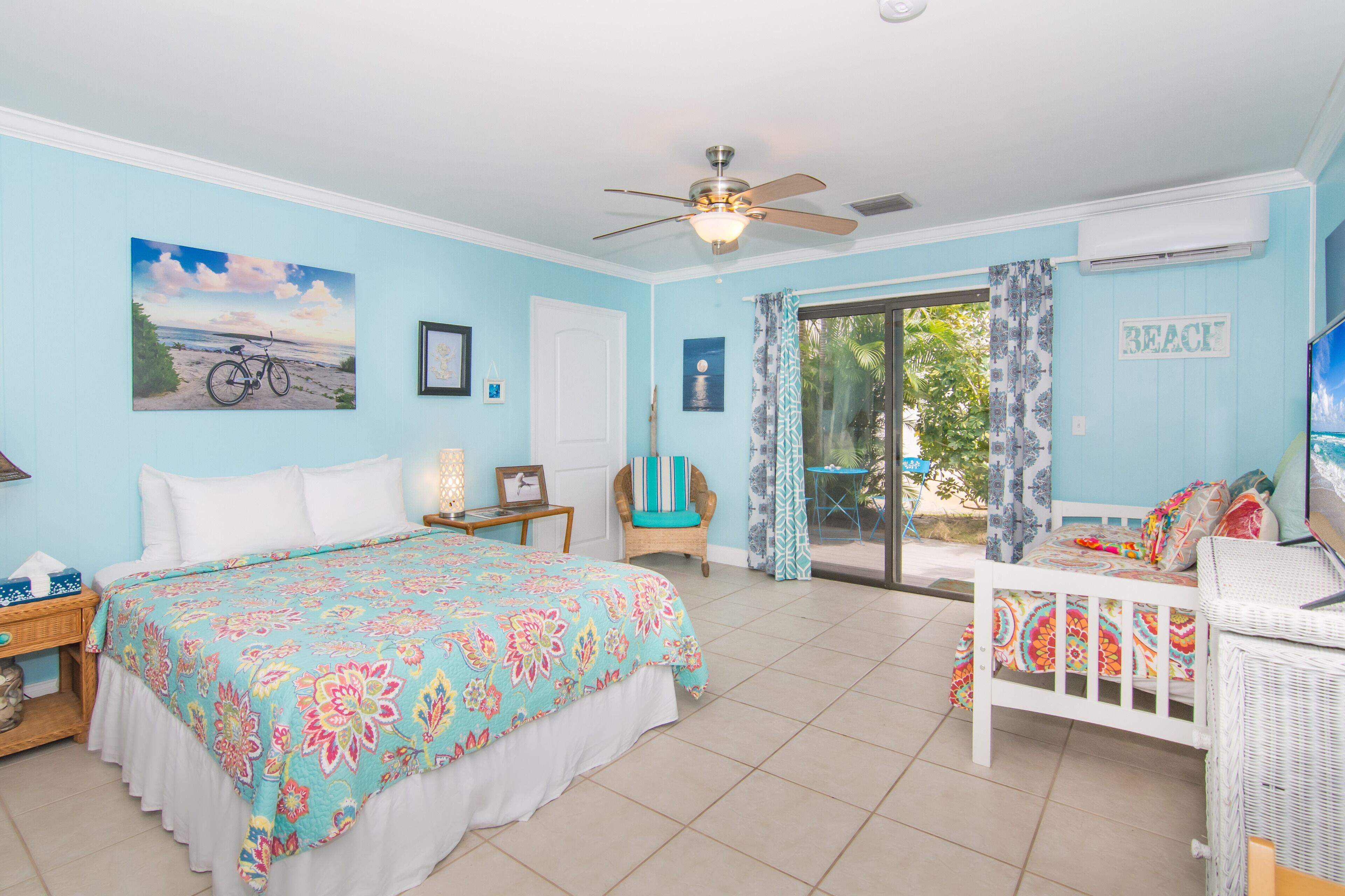 A bedroom with a bed, a chair, a ceiling fan, and a view of the outdoors.