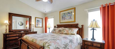 A bedroom with a wooden bed, a ceiling fan, a large mirror, and a window with curtains.