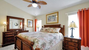 A bedroom with a wooden bed, a ceiling fan, a large mirror, and a window with curtains.