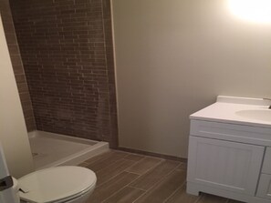 A bathroom with a white toilet, a shower area with a brick wall, and a white vanity with a sink.