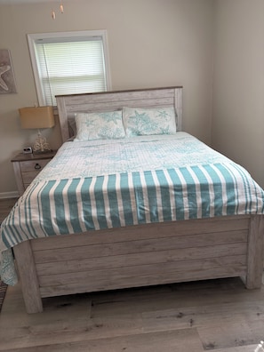 A bed with a striped bedspread, a wooden headboard, and a nightstand with a lamp and a clock.