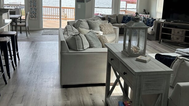 A spacious living room with a large sofa, a dining area with a table and chairs, and a television. There are large windows offering views of the water. - *** NEWLY RENOVATED**** Escape to a Beautiful Getaway on the Chesapeake Bay (Perryville)