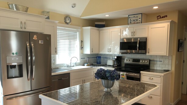 A modern kitchen with stainless steel appliances, white cabinetry, and a granite countertop.