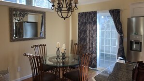 A dining area with a glass table, metal chairs, a chandelier, a large mirror, and a water dispenser.