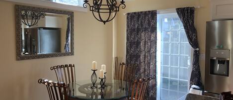 A dining area with a glass table, metal chairs, a chandelier, a large mirror, and a water dispenser.